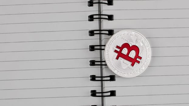Digital currency physical silver bitcoin coin with red sign in notebook.