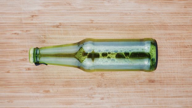 Tasty and fresh beer in green glass bottle on the wooden board in the kitchen.