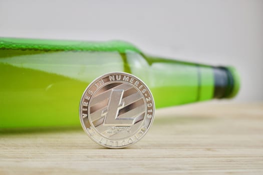 Digital currency silver Litecoin coin near green beer bottle. Drink concept.