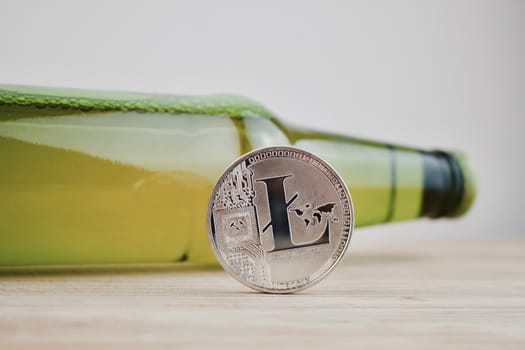 Cryptocurrency physical silver Litecoin coin on the wooden board near green bottle with beer.