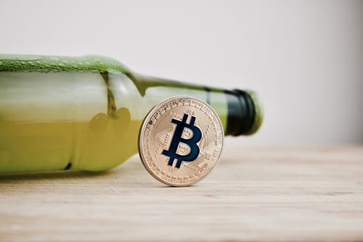 Digital currency physical gold bitcoin coin on the wooden board near green beer glass bottle.