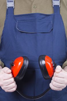 Protective headphones in the hands of a worker in blue overalls