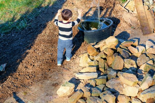Little boy throwing a stone into a water barrel