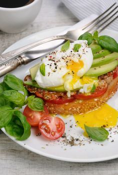 Egg poached on a toasted slice of baguette with tomato, spicy ham and avocado, sprinkled   spices and basil
