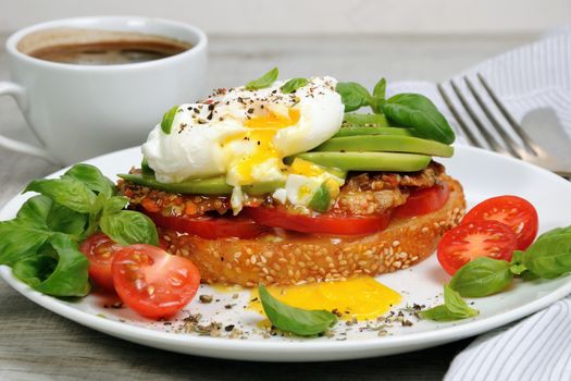 Egg poached on a toasted slice of baguette with tomato, spicy ham and avocado, sprinkled   spices and basil