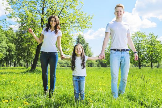 Cheerful family in summer sunny park walking on grass