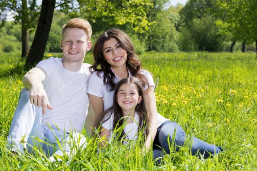 Cheerful family in summer sunny park sitting on grass