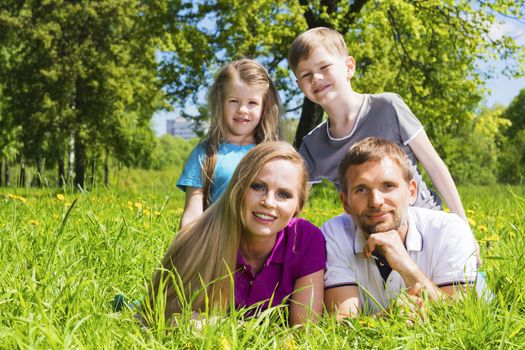 Father, mother and their children are lying on the green grass in the summer park