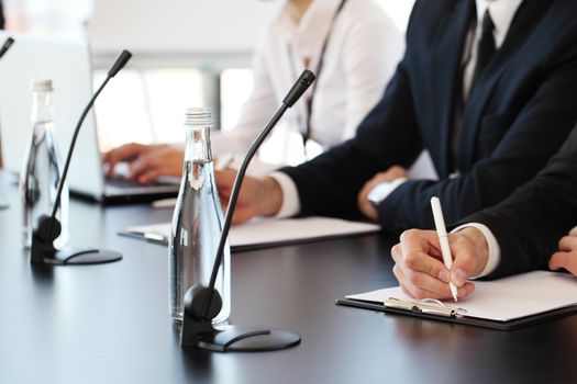 Group of speakers at business meeting at the table with microphones