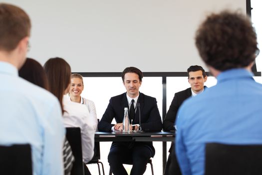 Group of speakers at business meeting at the table with microphones