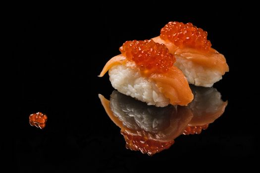 Sushi and red caviar on black acryle with reflection
