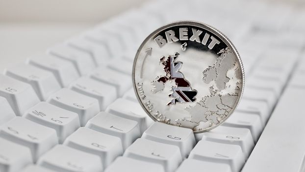 Europe leaving. Brexit physical coin on the white keyboard. British map.