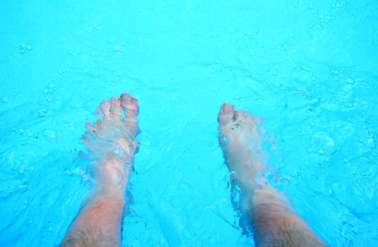 Top view on the feet refreshing in a clear water in the swimming pool.