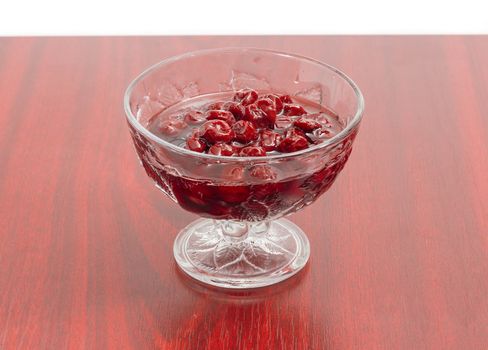 Cherry jam with whole fruits in the glass dessert stem bowl on a red wooden table
