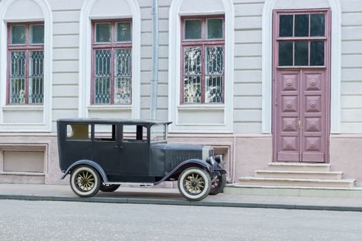 Black vintage car on a city street on the background of a facade of house with entrance door
