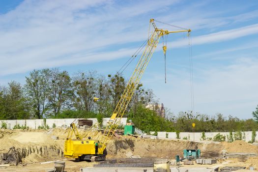 Yellow crawler self-propelled crane with latticed boom on the construction site during construction of the reinforced concrete basement of a building
