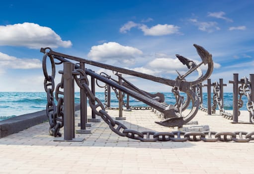 Several old anchors and anchor chains on the background of the sea and sky with clouds
