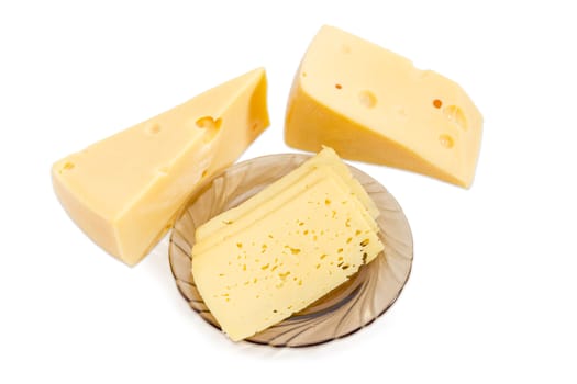 Semi-hard cheese cut into thin rectangular slices on the dark glass saucer and two pieces of the Swiss-type cheese beside on a light background
