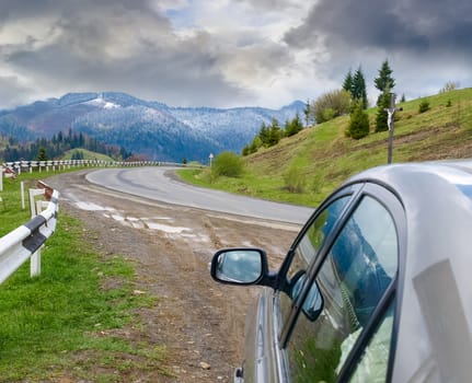 Section of the mountain road in the Carpathians with fragment of the car in the foreground in springtime after a rain with a snow
