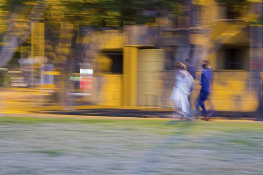 Newlyweds walking in the park at night with photographer. Bride and groom in a Sydney park hurrying toward a photo location.