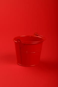 One small red painted metal empty toy bucket over red paper background, close up, high angle view