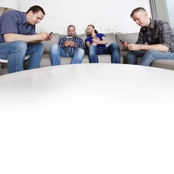 Four happy male friends using their mobile phones sitting on a sofa at home