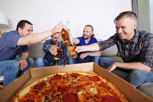 Male friends sitting at home on couch, clink beer, going to eat pizza, celebrating something