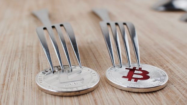 Cryptocurrency physical litecoin coin and bitcoin with fork on wooden board.
