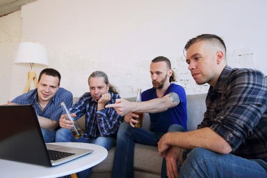 Male friends sports fans watching loosing football match on laptop at home on couch sharing snacks drinking beer