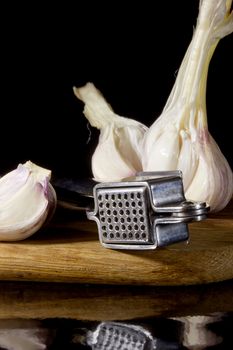 Garlic press and cloves of garlic laid on a wooden table background