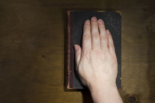 Female hand on the Bible on an old wooden background