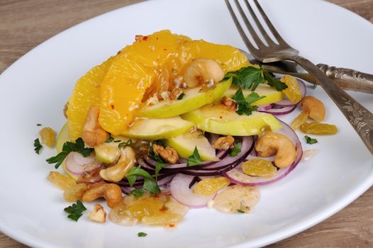 Salad with slices of orange, apple, blue onion, raisin, nuts, cashew nuts, herbs and honey sauce