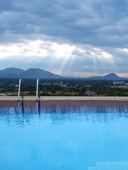 Outdoor swimming pool with sunbeam over mountains