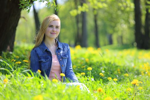 Beautiful young woman sitting in spring park with dandelion flowers