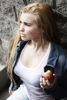 Urban style portrait of young beautiful blond woman in denim with apple