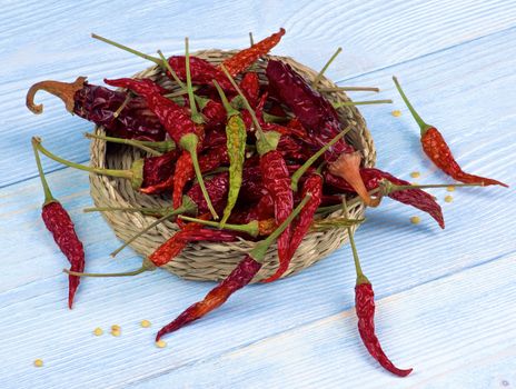 Heap of Dried Chili Peppers Full Body with Stems  and Seeds in Wicker Bowl closeup on Light Blue Wooden background