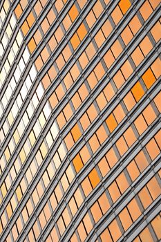 Orange colored glass windows of modern business office building at sunset in evening, diagonal perspective, low angle view