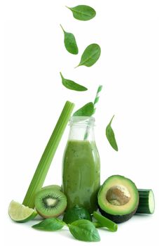 Leafy green greens falling into a smoothie bottle over a white background