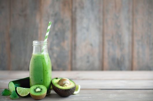 Green smoothie in a bottle with ingredients over a wooden background