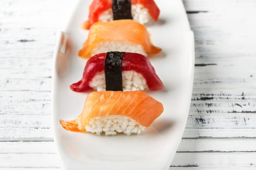  Set of salmon and red tuna Nigiris on white plate over old white wood. Raw fish in traditional Japanese sushi style. Horizontal image.