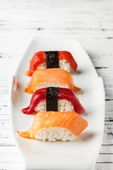  Set of salmon and red tuna Nigiris on white plate over old white wood. Raw fish in traditional Japanese sushi style. Vertical image.