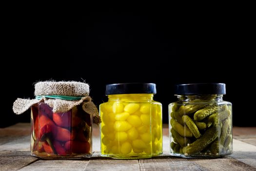 Mortar, vegetables in jars for the winter, wooden table in the old kitchen. Black background.