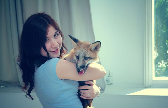 A beautiful smiling girl is holding a fox puppy in her hands.