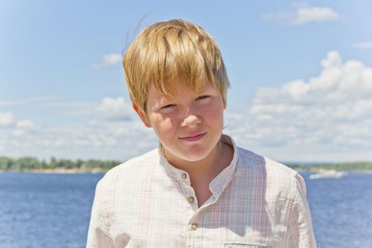 Portrait of squint blond boy in a white shirt near river