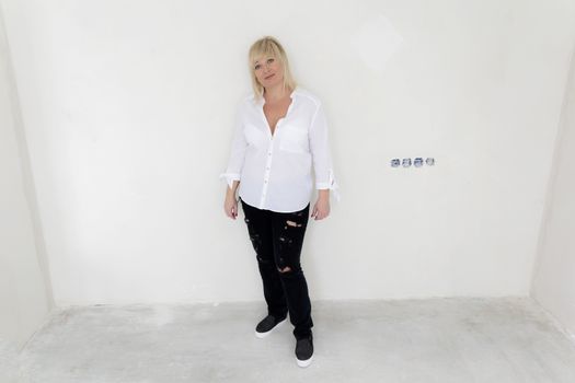 Blond woman in white and black jeans stand inside empty room