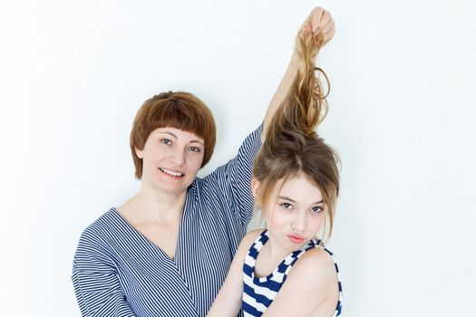 Mother and daughter playing with blond long hair near white wall