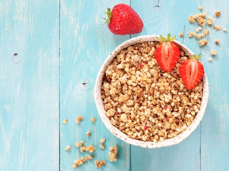 Top view of bowl with muesli and fresh strowberry on blue wooden background. Copy space.