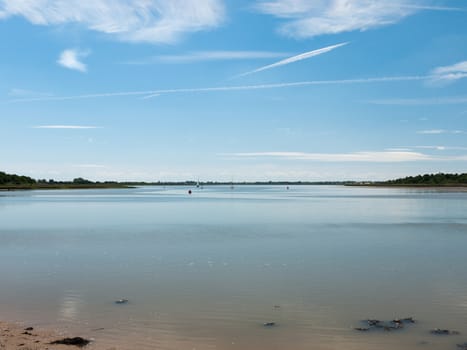 a calm and clear day on a river surface with country in the distance and buoys and boats no people beautiful