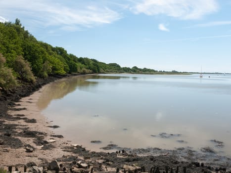 a calm and clear day on a river surface with country in the distance and buoys and boats no people beautiful and a bay with sand and rocks