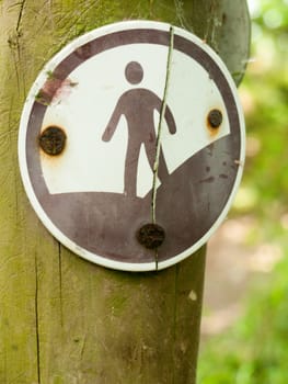 a rusty black and white sign with a man on it representing a country walking footpath